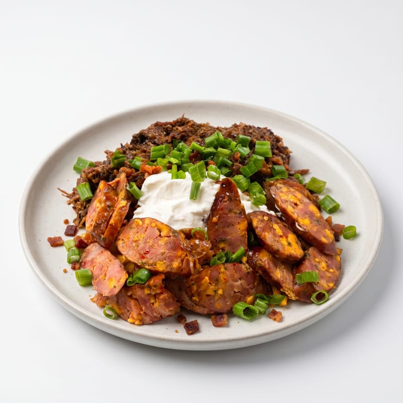 A plate of shredded beef, sliced sausage, sour cream, and green onions on a white background.